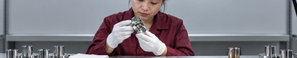 Plating technician in white gloves inspects a finished metal flange at a workbench, illustrating visual part evidence that can disagree with lab chemistry and process trend readings.